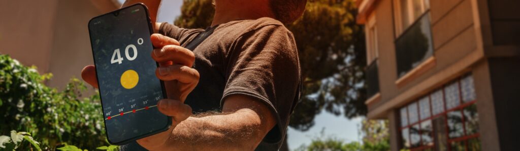 persona accaldata che tiene tra le mani un telefono sul cui schermo compare la temperatura di 40 gradi